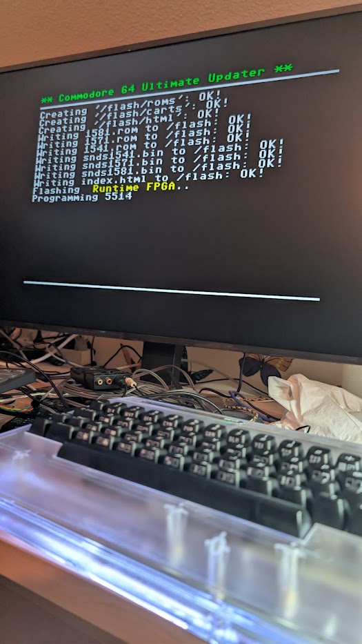 Photo of an HDMI screen showing the Commodore 64 Ultimate Updater writing files: 'Creating /flash/roms/: OK!', 'Writing 1571.rom to /flash: OK!', and 'Flashing Runtime FPGA.. Programming 5514'.